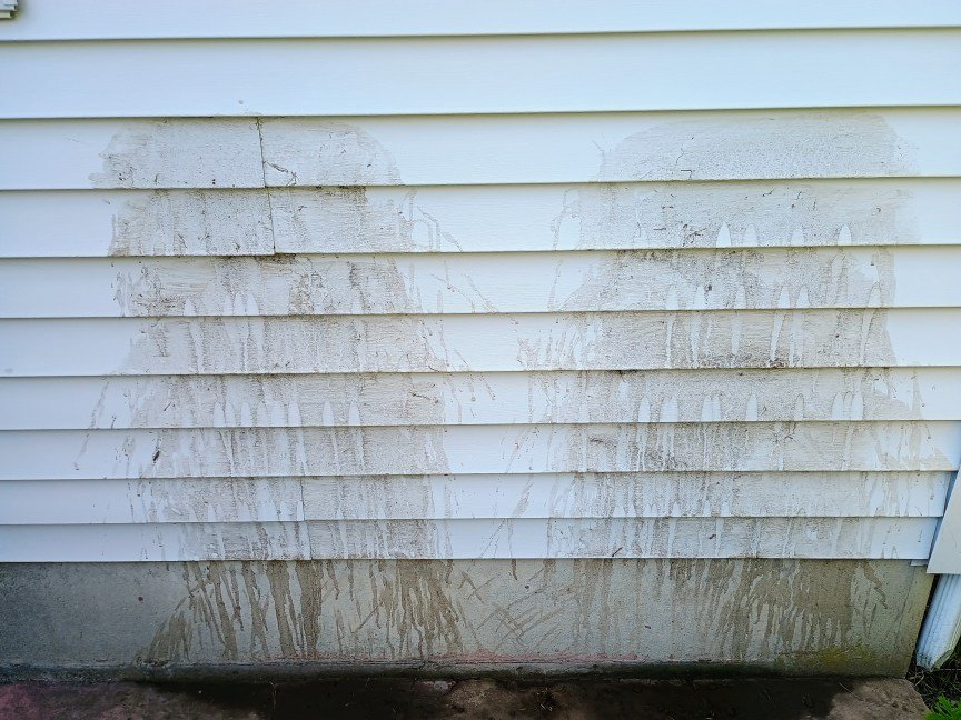 Two areas of light-colored house siding are covered in a mud slurry before being used to test power washers.