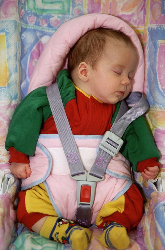 A baby sits in colorful 1990s child seat with a safety harness.