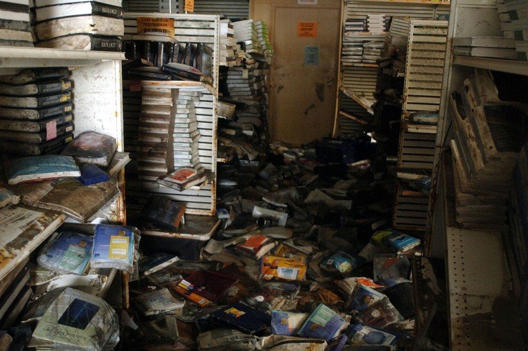 A large amount of damaged books are scattered across a floor and shelves with signs of flood damage.