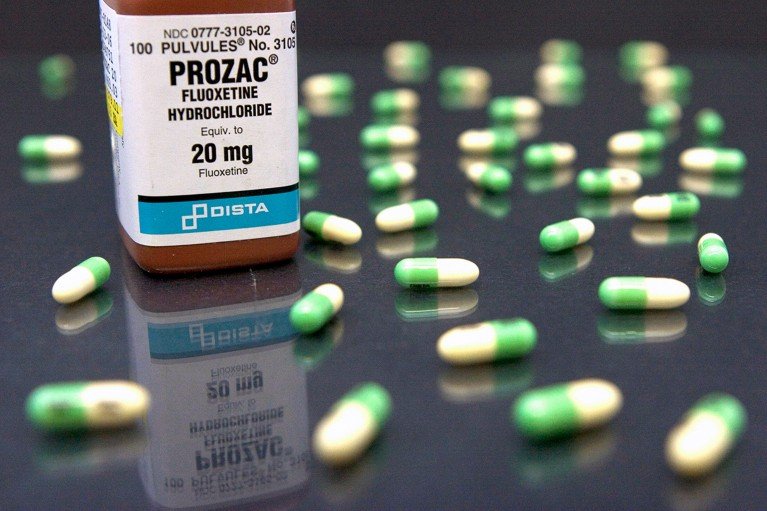 A bottle of Prozac capsules standing on a reflective surface with loose capsules scattered around.