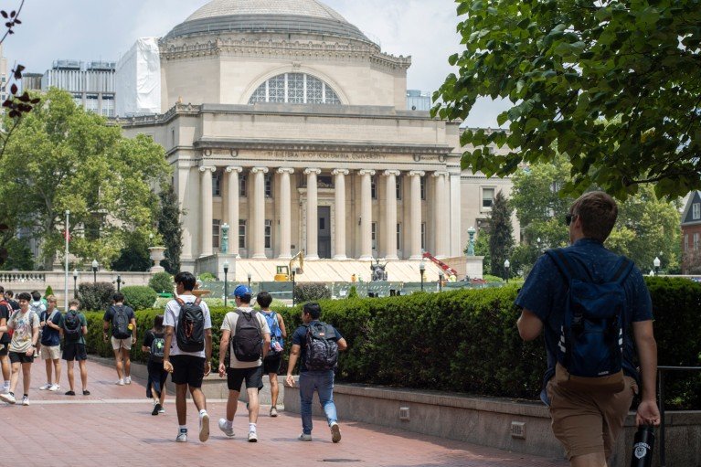 Students walk toward a large columned library building on a tree-lined university campus