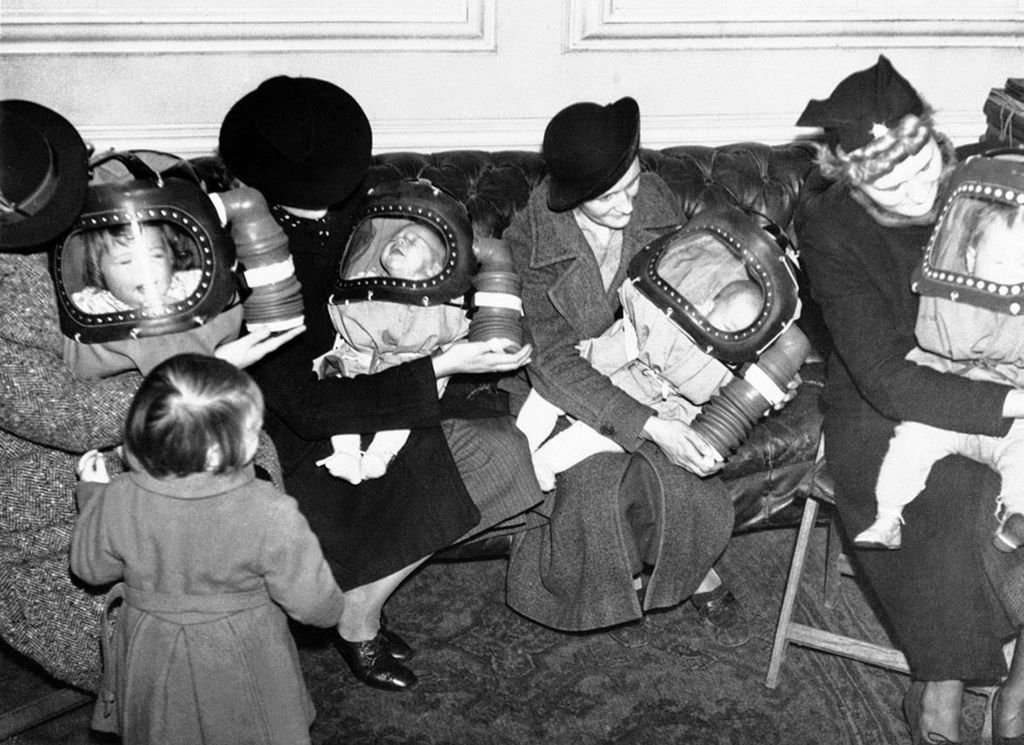 Four women hold their babies in hooded gas masks. 