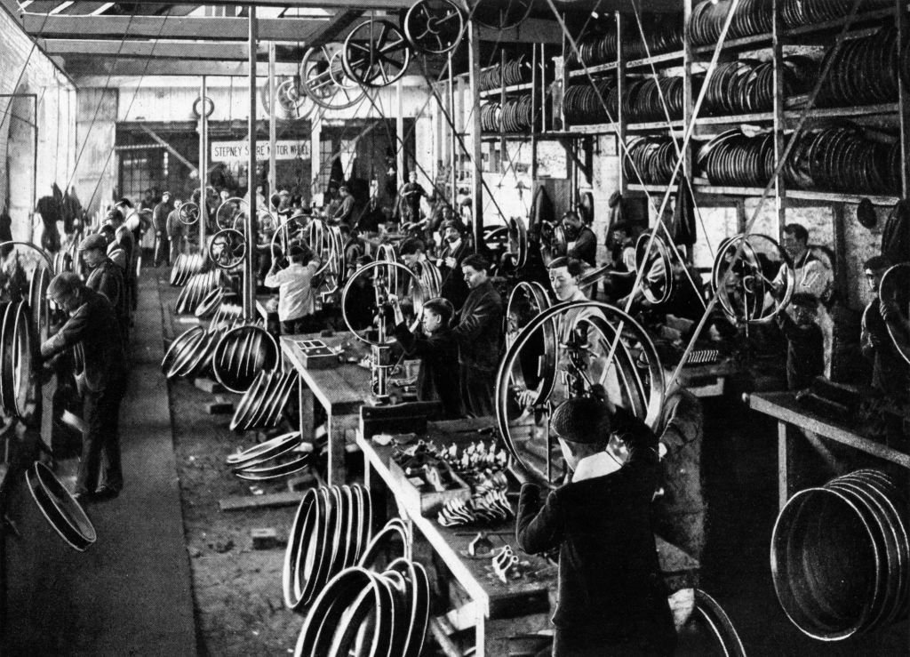 Workers busy producing wheel rims in vintage black and white photograph of a factory.