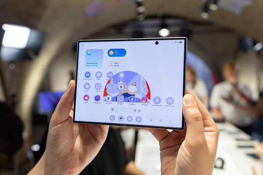 A foldable phone being held up in front of a busy room.