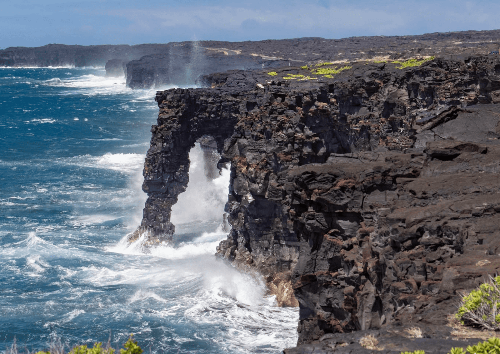 an arch made of volcanic rock with waves pounding at its base